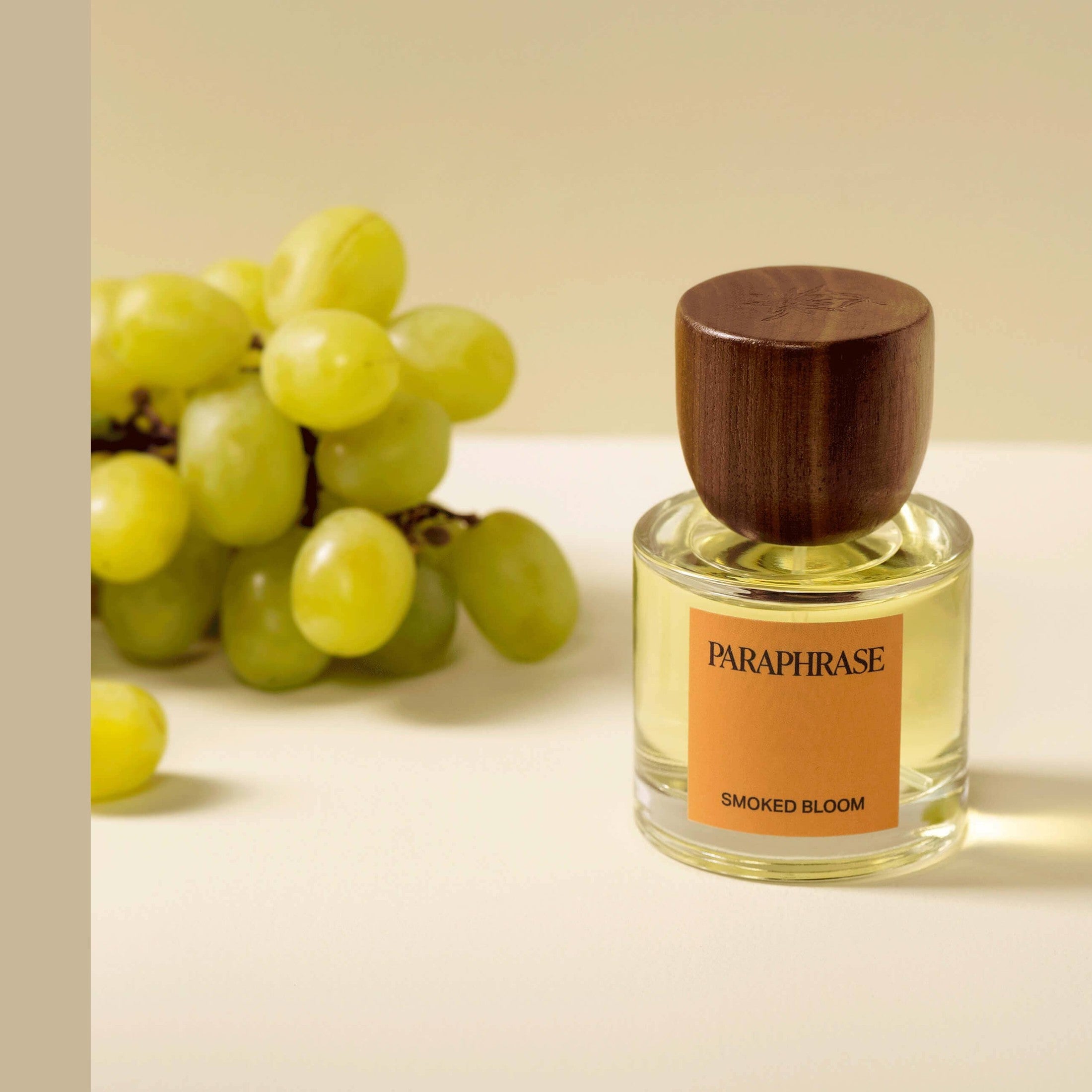 Smoked Bloom perfume bottle beside green grapes on beige surface