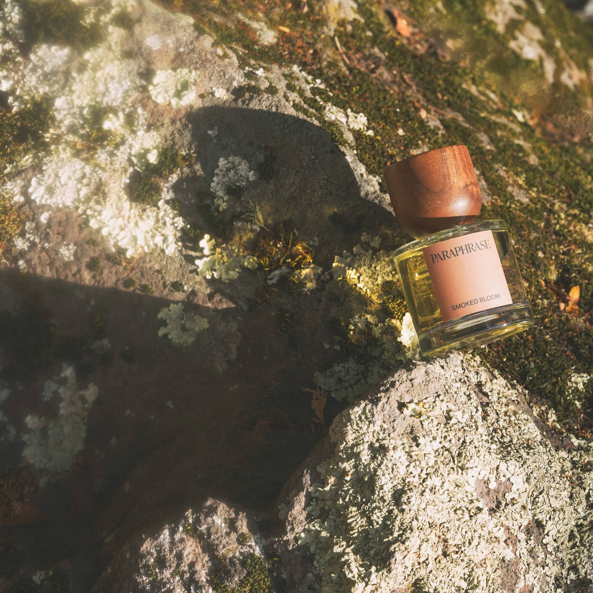 Paraphrase Smoked Bloom Eau de Parfum on mossy rock with golden liquid