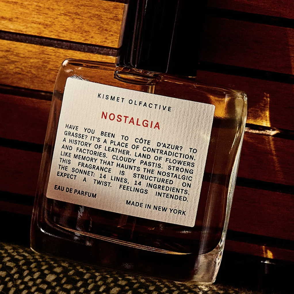 Close-up of Kismet Olfactive Nostalgia perfume bottle on dark wood showing red label text