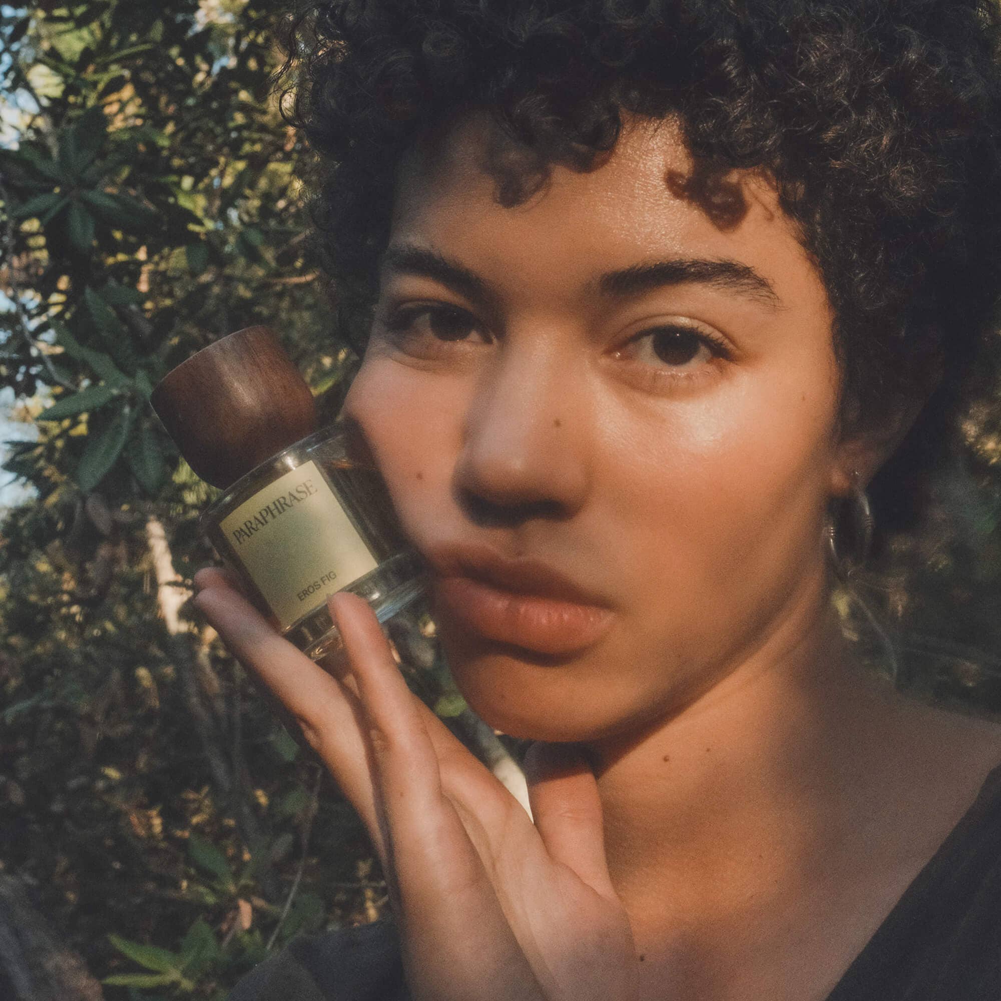 Paraphrase Eros Fig Eau de Parfum held by person with green foliage background