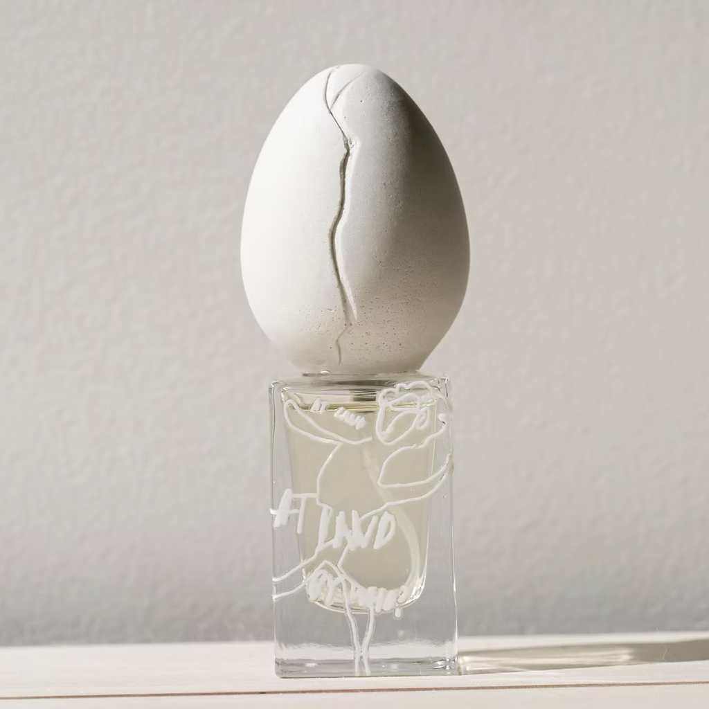 Perfume Who - At Land. White egg-shaped object on top of a clear glass container against a light gray background