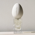 Perfume Who - At Land. White egg-shaped object on top of a clear glass container against a light gray background