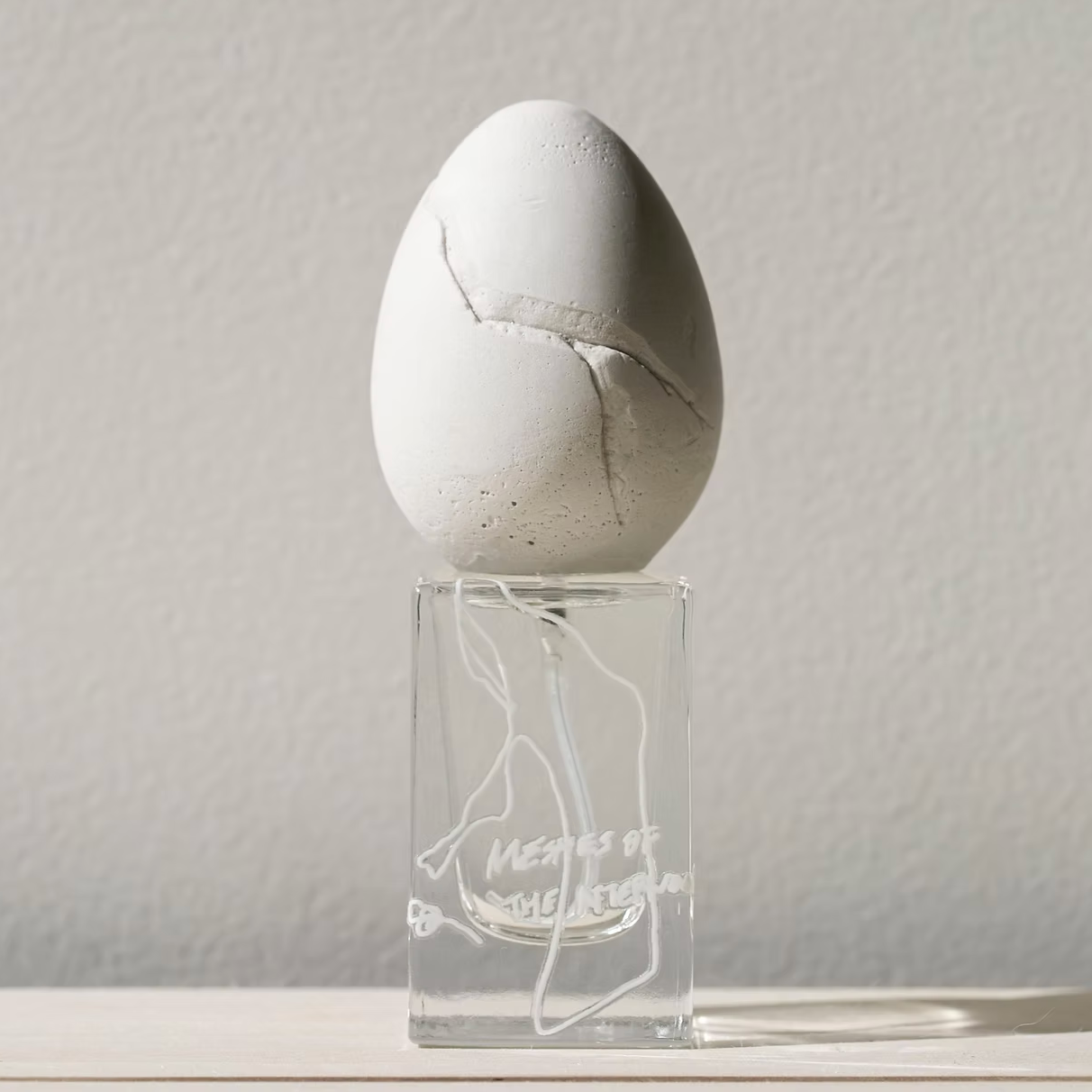 perfume who - meshes of the afternoon. Concrete egg on a clear stand with a subtle design against a light gray background
