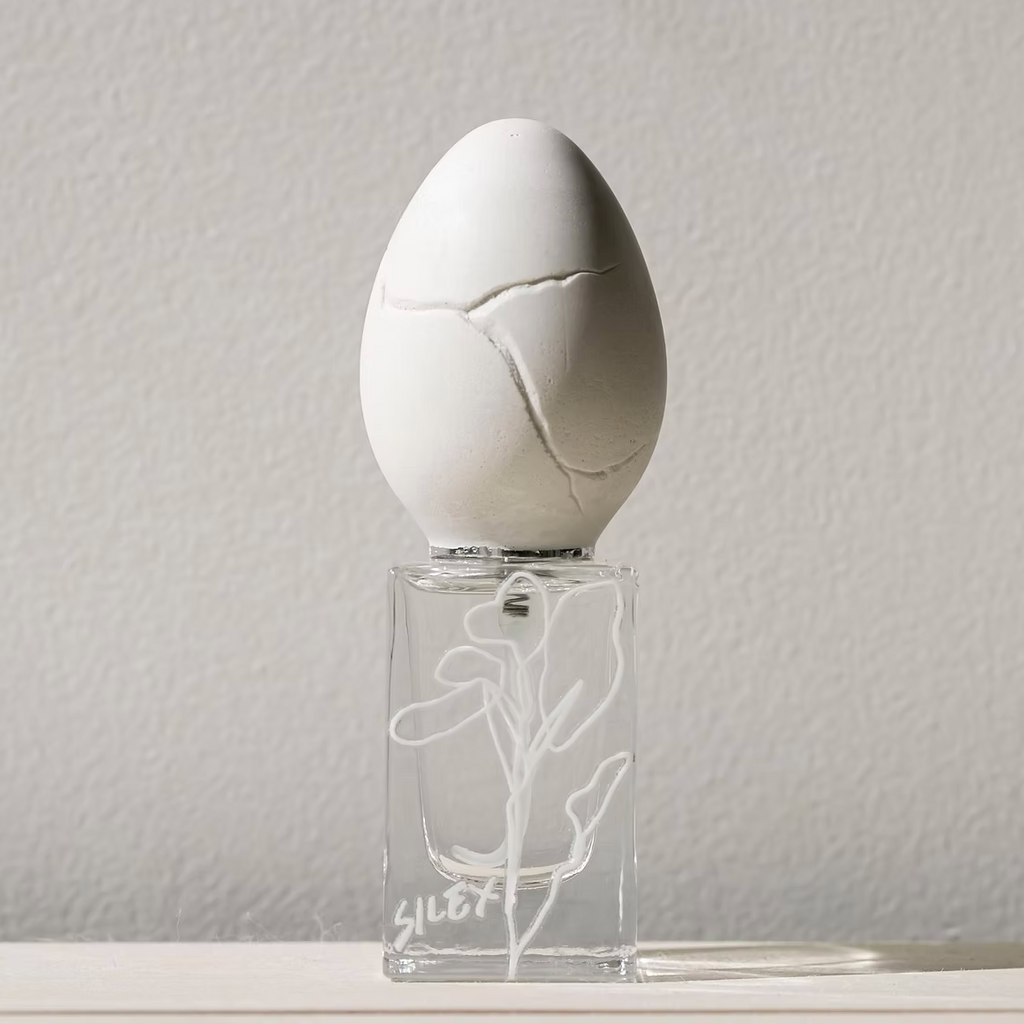 perfume who - silex. White egg-shaped object on a clear stand with a subtle design against a plain background