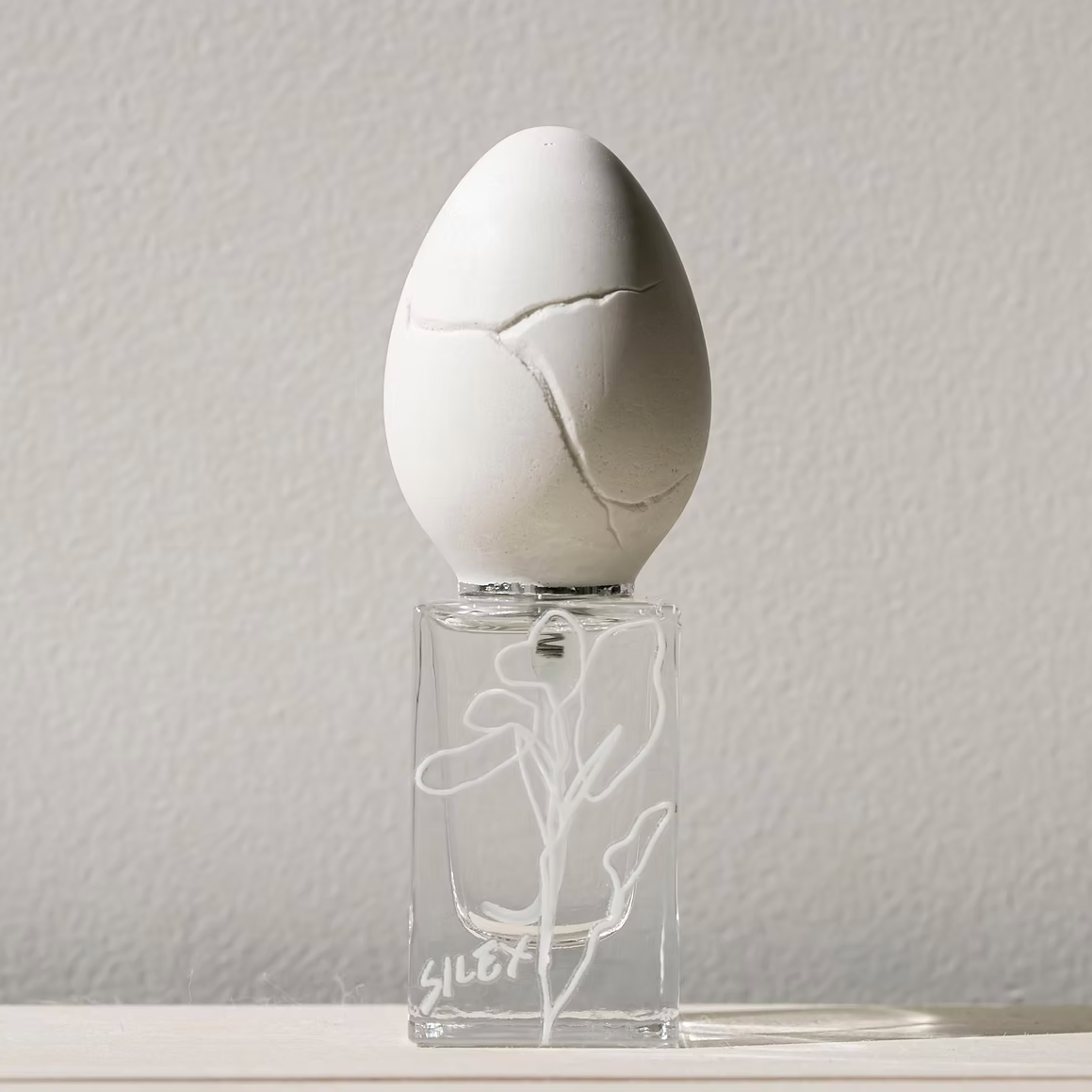 perfume who - silex. White egg-shaped object on a clear stand with a subtle design against a plain background